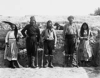 Five workers, three men and two women, stand in a row before an excavated stone wall at Vouni, with a dog resting behind them.