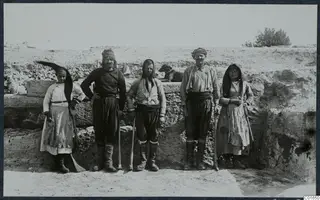 Workers from Tillyria, three men and two women, standing before a stone wall at Vouni, with a dog resting behind them.