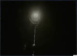 Dark view up or down an excavated opening, with a bright light at its centre and a white cord hanging down the middle