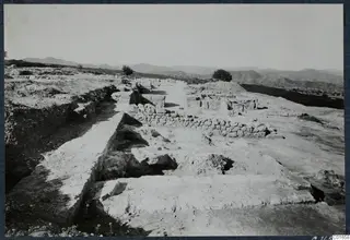 Excavated area at Vouni Palace with low stone walls, a cut rock edge and a trench, with hills behind