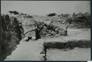 Finds in situ at Vouni Palace: a broken large vessel standing in an excavated trench beside a stone wall