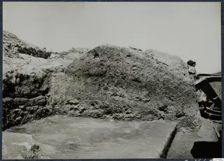 Large earthen wall beside a smooth pale floor at the Vouni palace, with a person and a wooden barrow at the right edge.