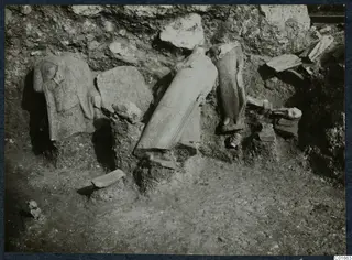 Stone sculptures and architectural fragments lying in excavated soil against a rock face at Vouni Palace.
