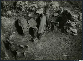 Statues and stone fragments lying in situ in an excavation at Vouni Palace, against a rock face