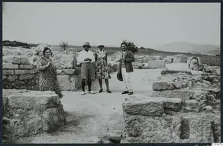 Four people standing among stone ruins at Vouni, with fields and hills behind them.