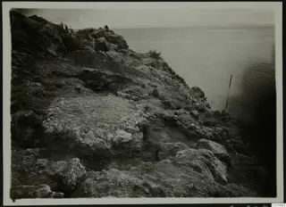 Excavated rocky slope at Petra tou Limniti with exposed stone walls running down toward the sea.