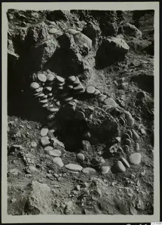 Rounded stones set in a curving line around a dark opening in rocky, excavated ground at Petra tou Limniti