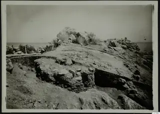 Excavation at Petra tou Limniti with a man seated among stones above the sea