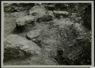 Excavated ground with large rough stones and a small pale object at Petra tou Limniti