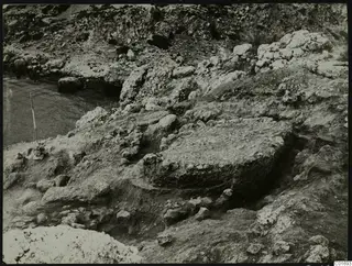 Excavation at Petra tou Limniti with rock ledges, rubble and water at the left edge of the view.