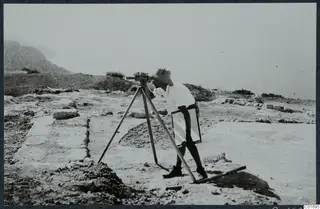 Alfred Westholm looking through a levelling instrument on a tripod, on stone-paved ruins at Vouni