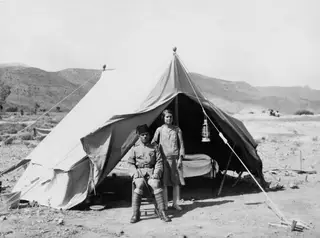 Policeman seated outside a tent at Ayios Iakovos, with a woman standing beside him
