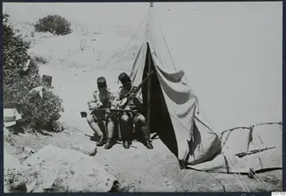 Two saptiena seated outside a tent at Vouni, handling rifles