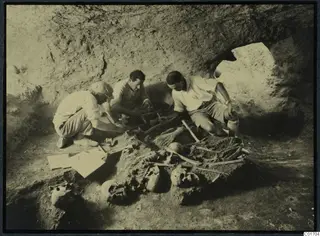 Three men kneeling beside a skeleton at Ayios Iakovos, cleaning the bones