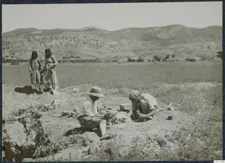 Two men packing skulls at the Ayios Iakovos excavation, with a shovel and a wooden box nearby
