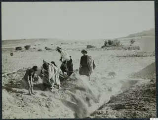 Workers shovelling soil into a trench at Ayios Iakovos, with a white tent and dry hills behind