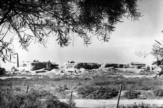 Bamboula mound at Kition seen from the east, with cut earth faces and several people standing and sitting on its top