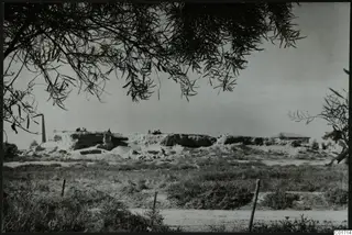 Bamboula at Kition seen from the east: a long eroded mound of earth and stone with several people standing on top