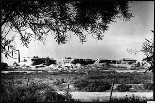 Bamboula at Kition seen from the east: a long mound with cut faces, with several people sitting on its top