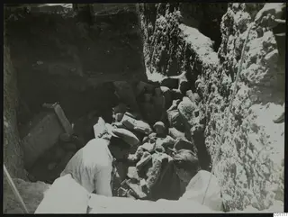 Two men digging among stone sculpture fragments and blocks in a deep trench at Kition