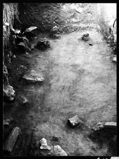Excavated room at Kition with stone blocks and rubble scattered over an earth floor, walls along two sides