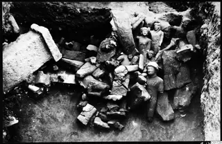 Large broken sculptures and stone fragments piled together in the great deposit of the cult room at Kition