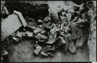 Excavation of the cult room great deposit at Kition, showing a heap of large broken stone sculptures in a trench