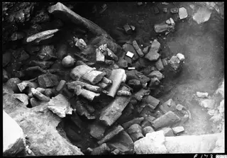 Excavation of the cult room deposit at Kition, with broken stone sculptures, bodies and heads among dark soil