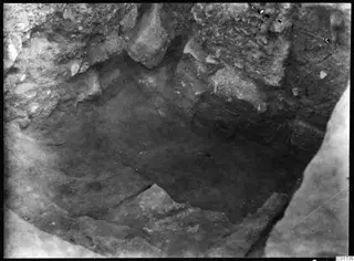 Excavation pit at Kition seen from above, with rough stone and rubble sides and a dark soil floor.