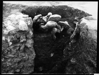Central pit at Kition with sculpture fragments lying in situ among stones, a taut string stretched across the trench