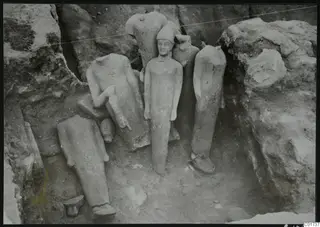 Statues in situ in the middle pit at Kition, with one standing figure wearing a conical cap