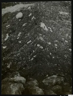 Soil profile in the northeast corner of the cult room at Kition, with pale flecks and large stones at its base.