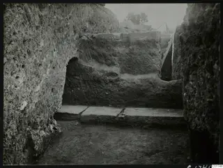 Large excavated profile wall of soil and stone inside a room at Kition, with flat stone slabs at its base