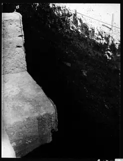 Deep excavation trench at Kition with a tall soil section on the right and a pale stone wall face on the left
