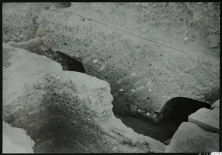 Excavated profile at Kition with dark openings at the base of a pale earth face, leading to galleries