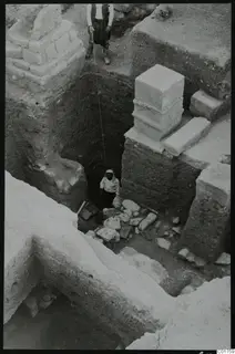 Deep excavation at Kition with a worker in the pit among scattered stones and stacked squared blocks beside the trench wall