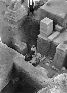 Deep excavation at Kition east of cult room I-III, with cut stone blocks and two men working in the trench