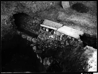 Roman water channel at Kition, stone-lined, with flat slabs laid over a rubble wall in an excavation trench.