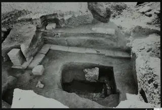 Excavated cult room at Kition seen from the north, with stone slabs along the back and a square pit with stones in it.