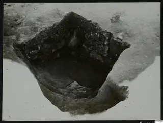 Excavated pit at Larnaca with an angular soil profile of dark earth and stones, seen from above