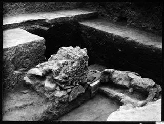 Excavation trench at Kition with a large rough stone mass in the centre and cut earth faces and ledges around it