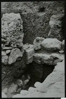 Excavation at Kition showing rough stone blocks, a small carved figure on a block, and a trench below.