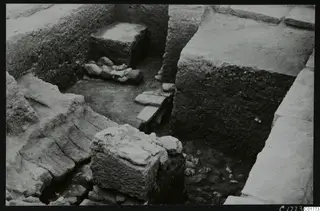 Excavated trench at Kition below the cult room, with a large squared stone block and earthen walls.