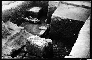 Excavation trench at Kition below the cult room, with stone walls, flat slabs and a square stone block in the foreground.
