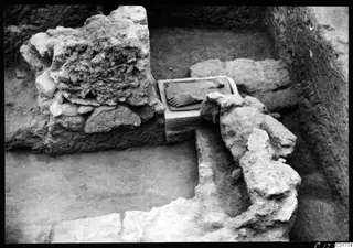 Excavation trench at Kition with a stone block carved in relief with a foot, beside rubble walls and fallen stones.