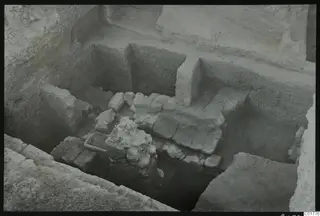 Excavated structures of walls and stone blocks in a deep trench at Kition, seen from above.