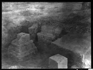 Stone pedestals uncovered during excavation at Kition, standing in a trench with earth banks around them.