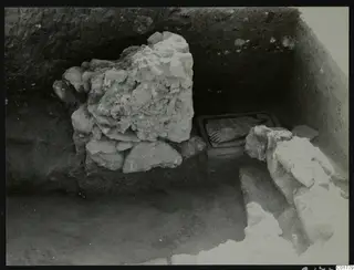 Excavation at Kition with large broken stones and a flat slab in a recess in the trench wall.