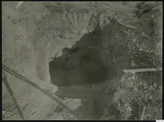 Excavated cut at Kountoura Trachonia with stones at the back of a dark hollow and a plank lying at the right edge