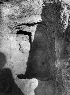 Tomb 7 at Kountoura Trachonia, exterior: a narrow cut leading to a dark tomb opening beside a large stone